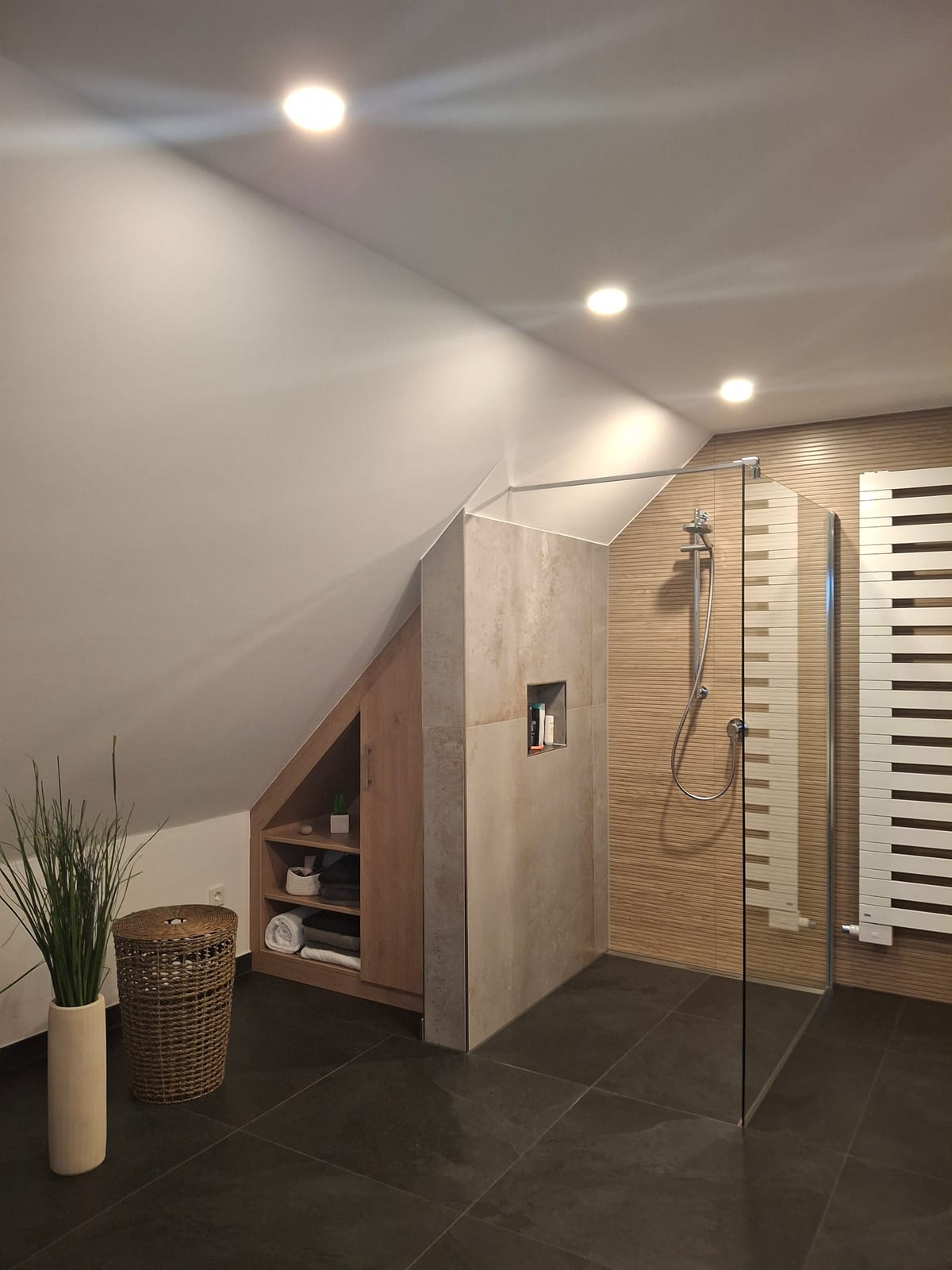 Bodengleiche Dusche mit Glasabtrennung und Holzoptik-Fliesen unter einer Dachschräge mit Handtuchheizkörper
